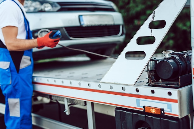Tow truck operator winching car onto flatbed truck.